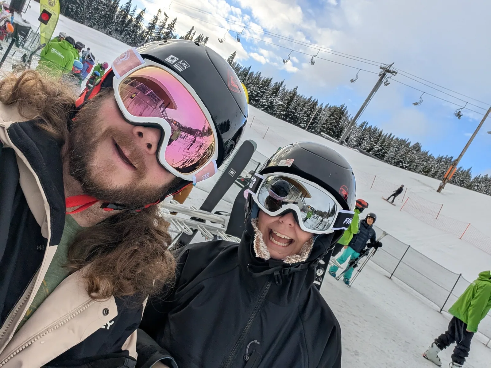 Levi and Natalie wearing ski helmets and goggles at a snowy ski area.