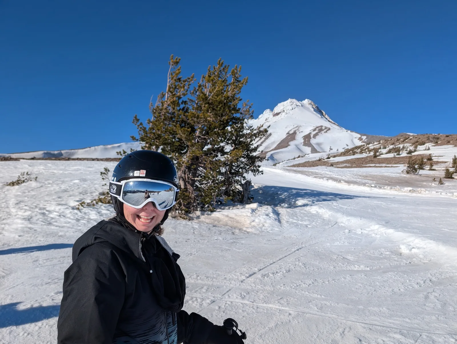 Natalie wearing a ski helmet and goggles on a sunny slope with Mount Hood behind her.