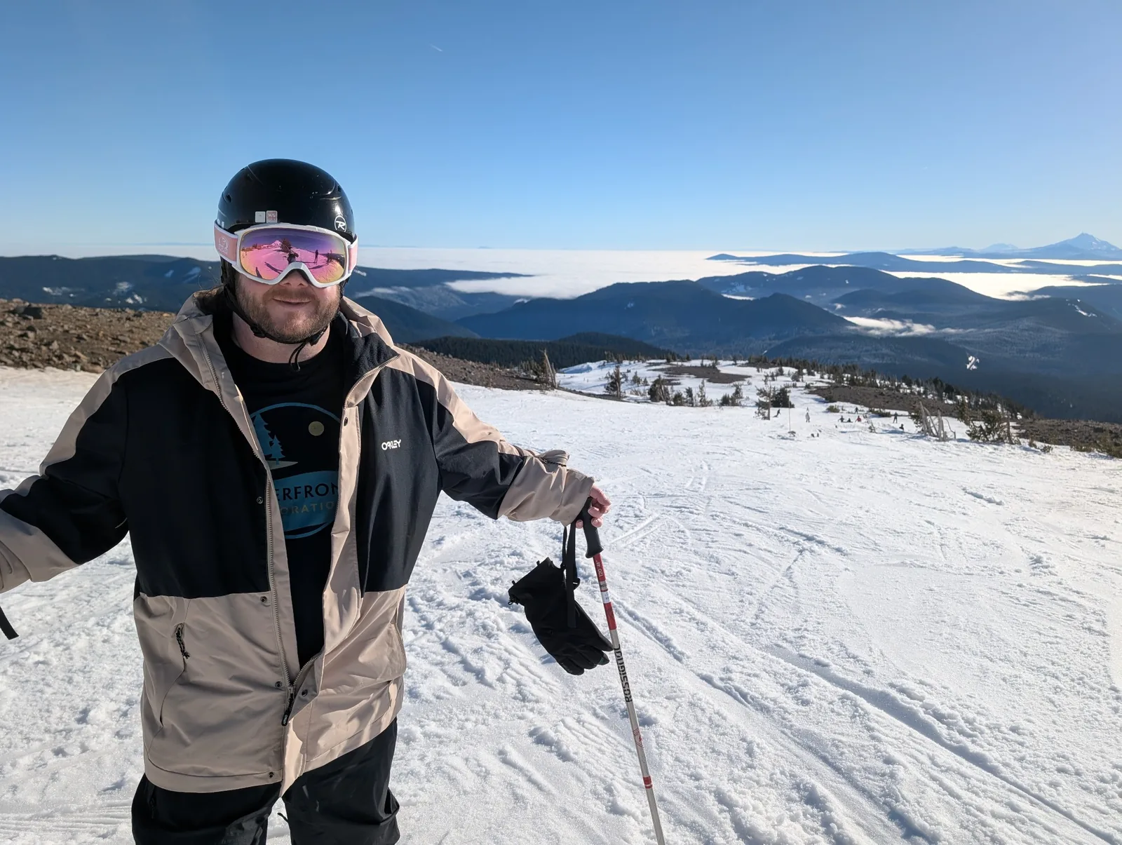 Levi holding ski poles on a snowy slope above forested ridges and low clouds.