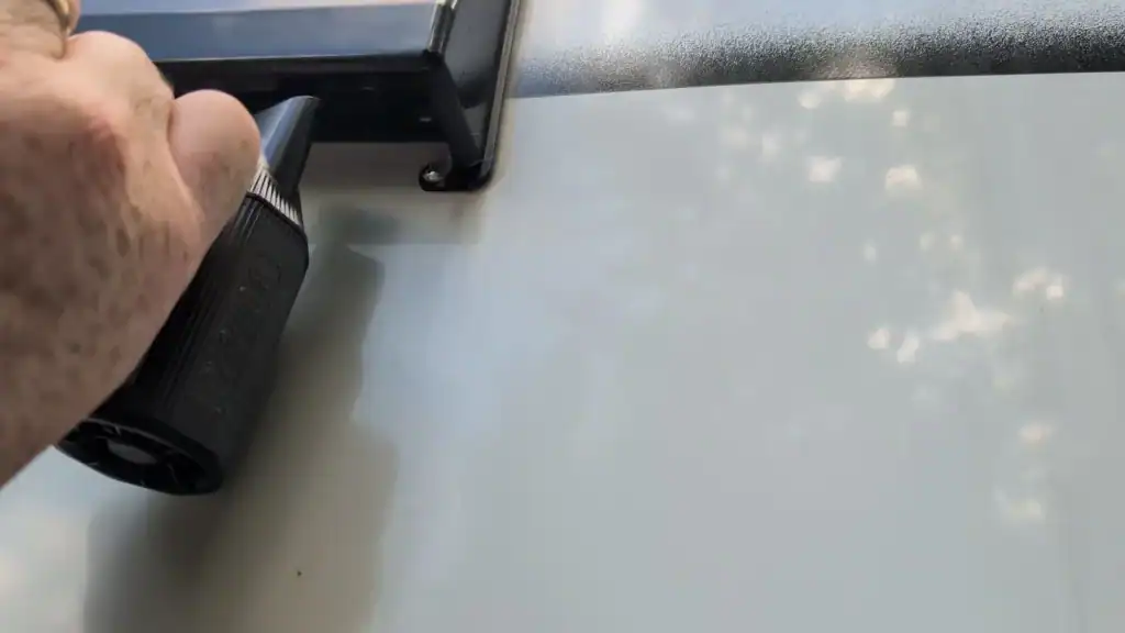 Hand holding a Blowzer air duster with its nozzle aimed into the RV’s exterior dryer vent opening.