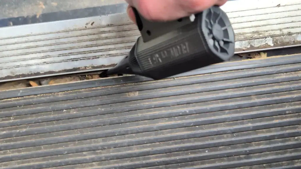 Hand holding a Sabrent Blowzer with its nozzle aimed along the grooved RV entry threshold.